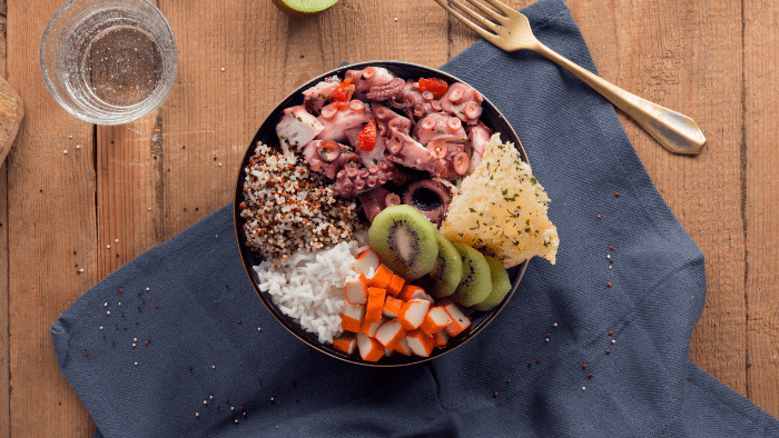 Poke bowl di riso con polpo, surimi, kiwi, semi di quinoa e chips di grana con prezzemolo